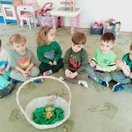 Dzieci siedzą na dywanie, a przed nimi stoi koszyk z żabą