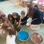 Nauczycielka wraz z dziećmi dotykają sztucznego mchu