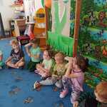 dzień przedszkolaka- dzieci siedzą na dywanie , chłopiec i dziewczynka patrzą przez lornetkę zrobioną z rolek po papierze